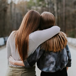 One young woman hugging another